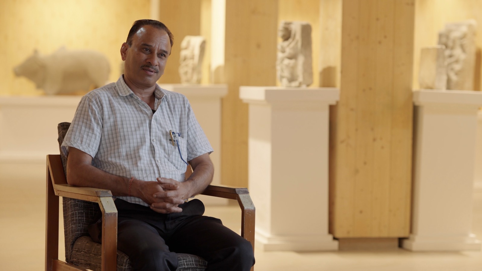 A historian seated in a museum gallery of carved stone sculpture