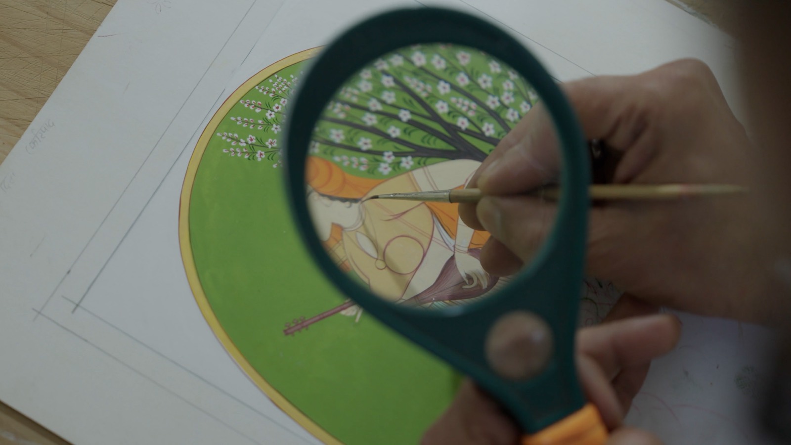 A magnifying glass held over a miniature as a fine brush adds blossom detail