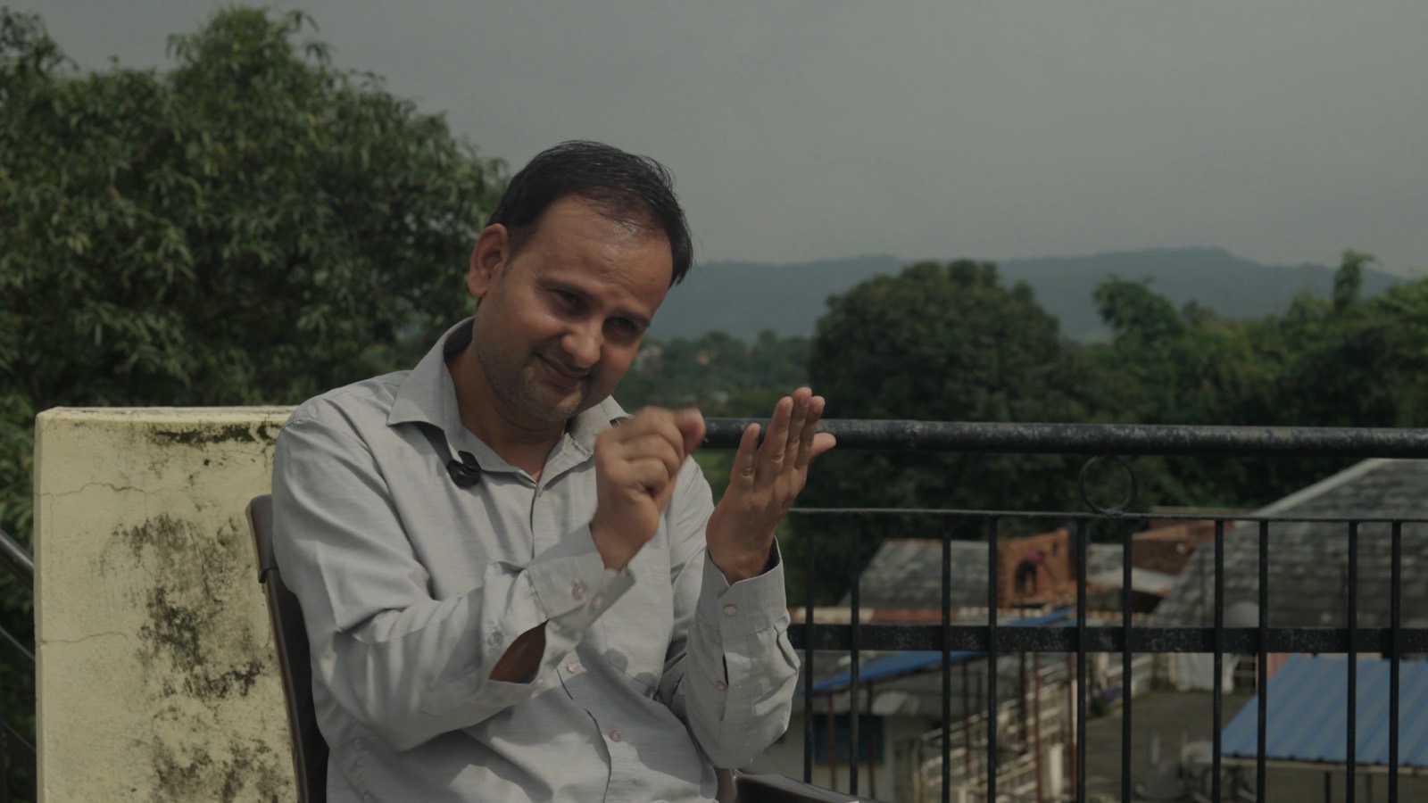 An artist signing while speaking to camera on a rooftop, hills behind him