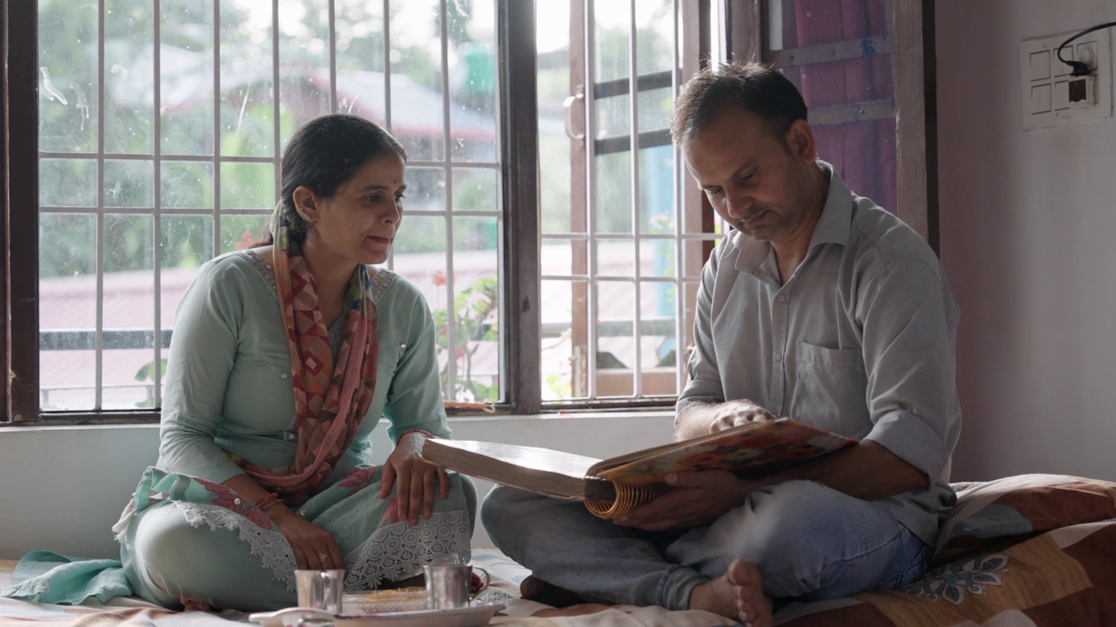 Two people seated on the floor at home, looking through a large book together